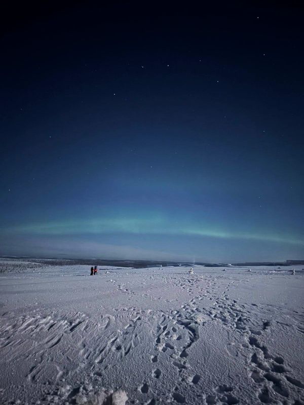 Schneelandschaft vor Nachthimmel mit grünem Polarlichtbogen und den Sternen des "Großen Wagen"
