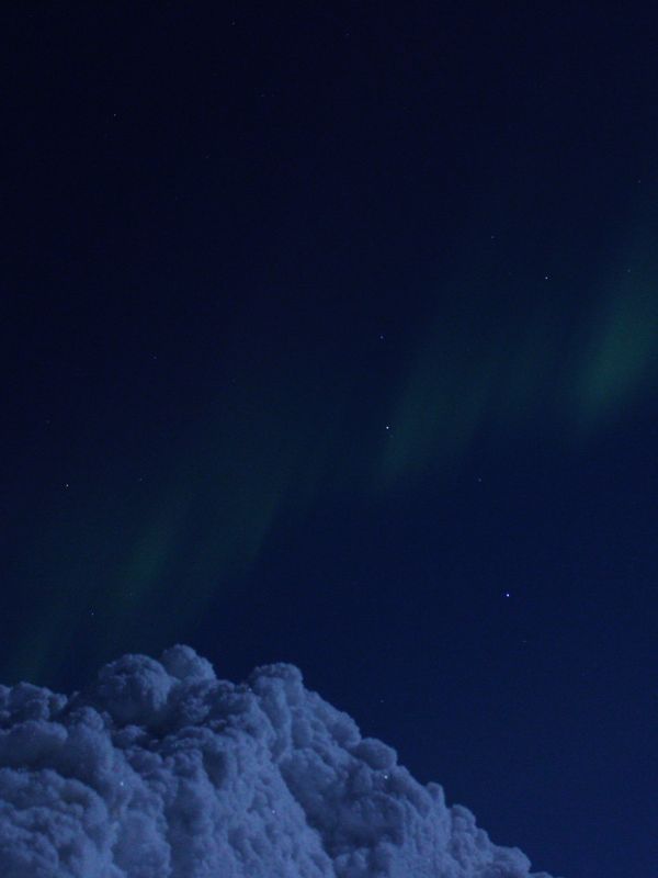 Schneehügel vor Nachthimmel mit grünem Polarlicht und den Sternen des Sternbildes "Löwe"