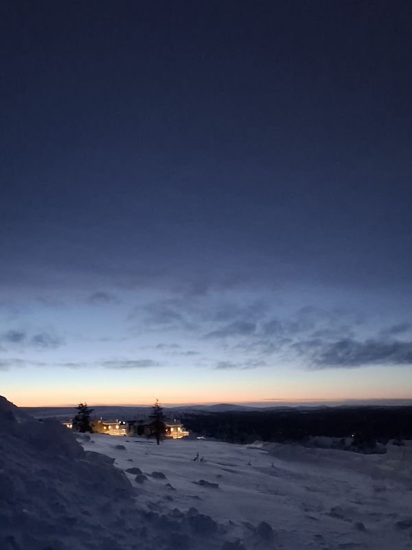 Schneelandschaft mit viel Himmel. Oben dunkelblau, langsam heller werdend und am Horizont ein dünner gelblicher Streifen.