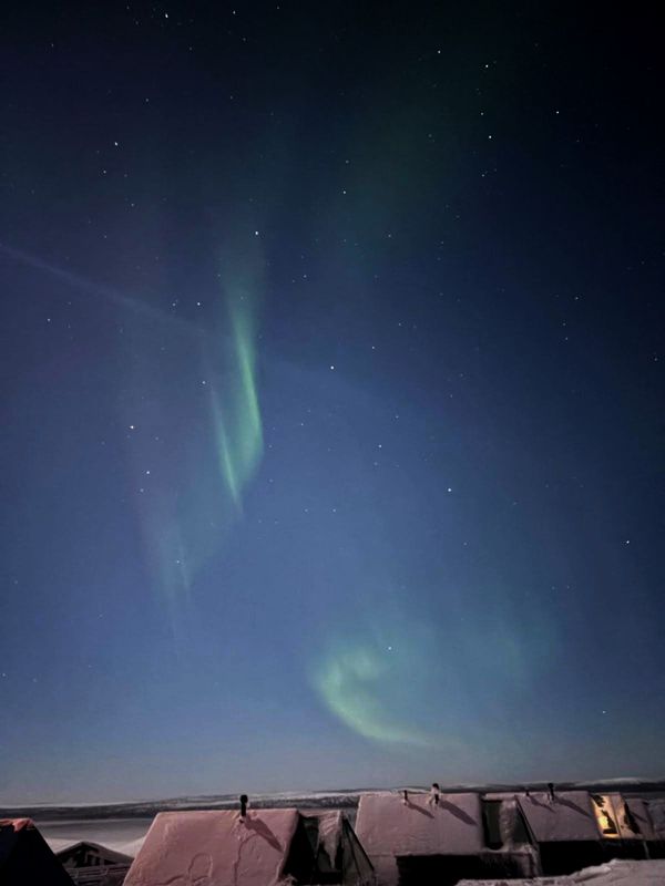 Schneelandschaft mit verschneiten Hütten und grünem und rötlichem  Polarlicht von oben nach unten 
