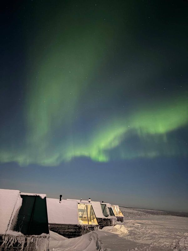Schneelandschaft mit verschneiten Hütten und grünem Polarlicht am gesamten Himmel